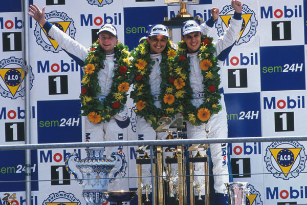 Allan McNish, Stéphane Ortelli, Laurent Aiello na podium przed logo Mobil 1 w Le Mans 1998