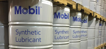 Beczki Mobil™ Synthetic Lubricant ułożone na paletach w uporządkowanym korytarzu magazynowym.